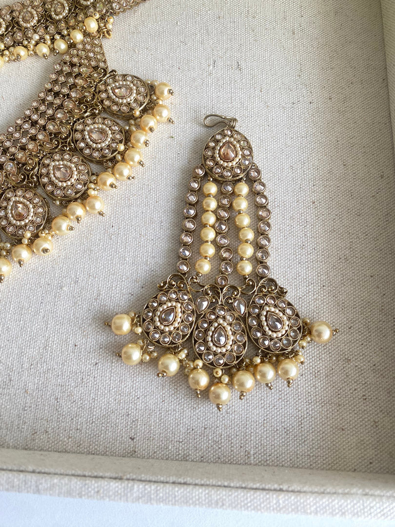  Festive Essentials - Anita Bridal Champagne set represents graceful set of jewellery which includes tikka, handset, mathapati, necklace, earrings, and jhumaar.Antique&nbsp; Gold base with champagne gold stone with maroon stone is perfect combination for any bride. Golden pearls or maroon pearls add beauty to this set. For Customization please contact us on whatsapp at +1 (313) 727 1045.