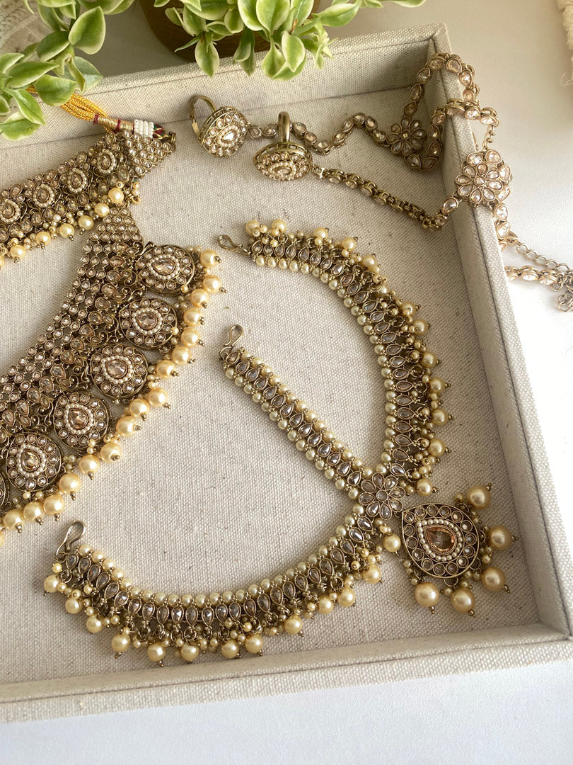  Festive Essentials - Anita Bridal Champagne set represents graceful set of jewellery which includes tikka, handset, mathapati, necklace, earrings, and jhumaar.Antique&nbsp; Gold base with champagne gold stone with maroon stone is perfect combination for any bride. Golden pearls or maroon pearls add beauty to this set. For Customization please contact us on whatsapp at +1 (313) 727 1045.
